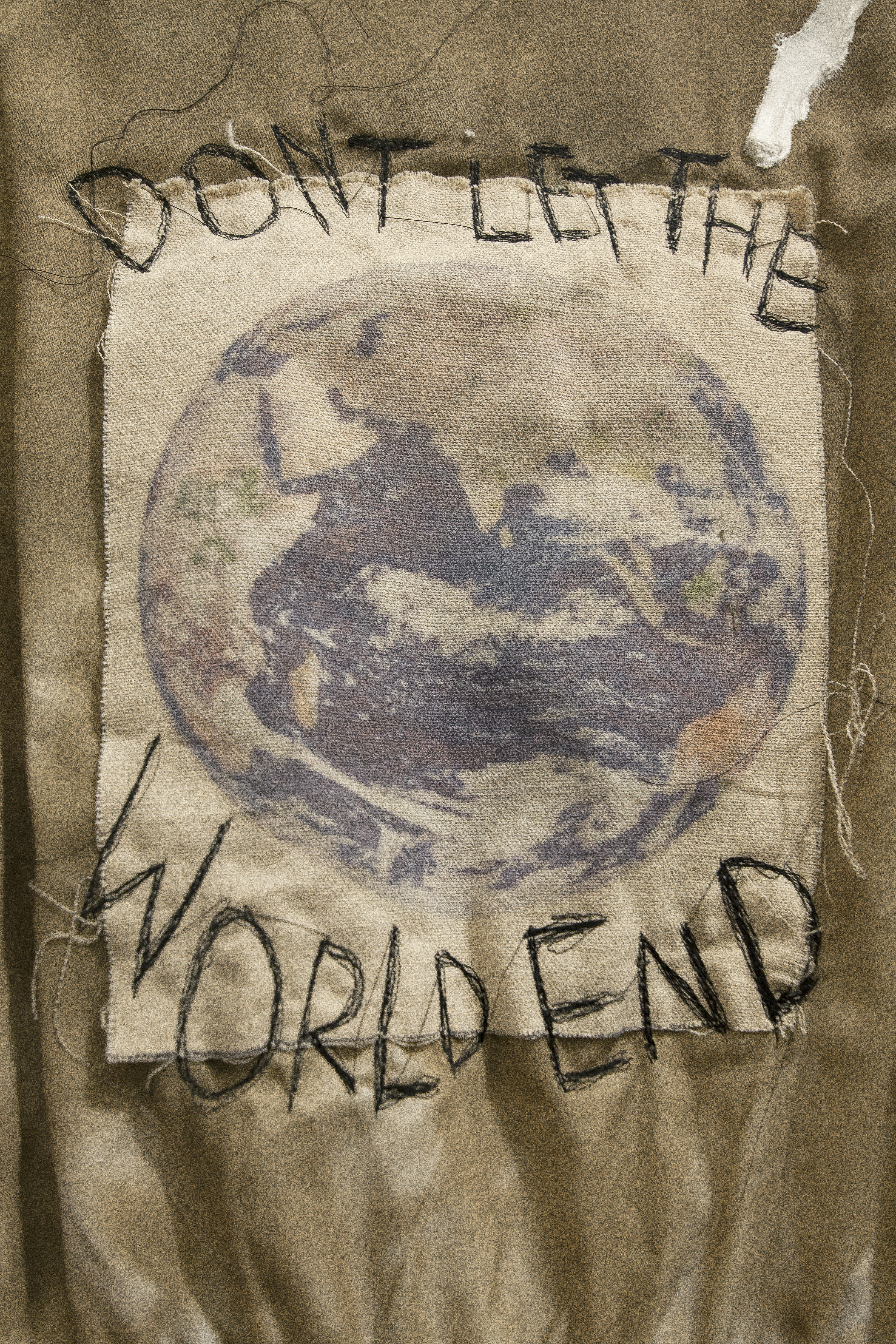 Detail of a patch with a print of the world on it sewn onto the back of a cream jumpsuit